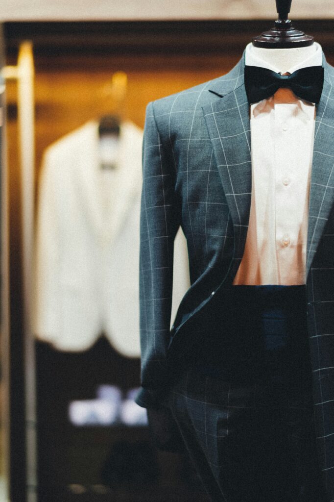 A formal black tie outfit displayed on a tailor's mannequin with a white dinner jacket blurred in the background.