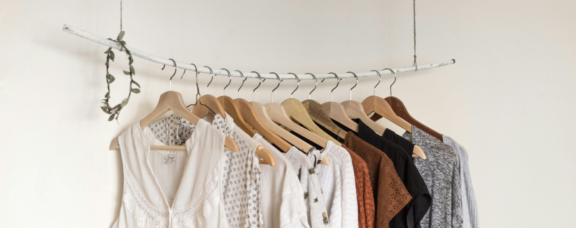 A collection of neutral-toned women’s clothing displayed on wooden hangers on a suspended white clothing rail.