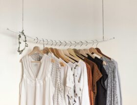 A collection of neutral-toned women’s clothing displayed on wooden hangers on a suspended white clothing rail.