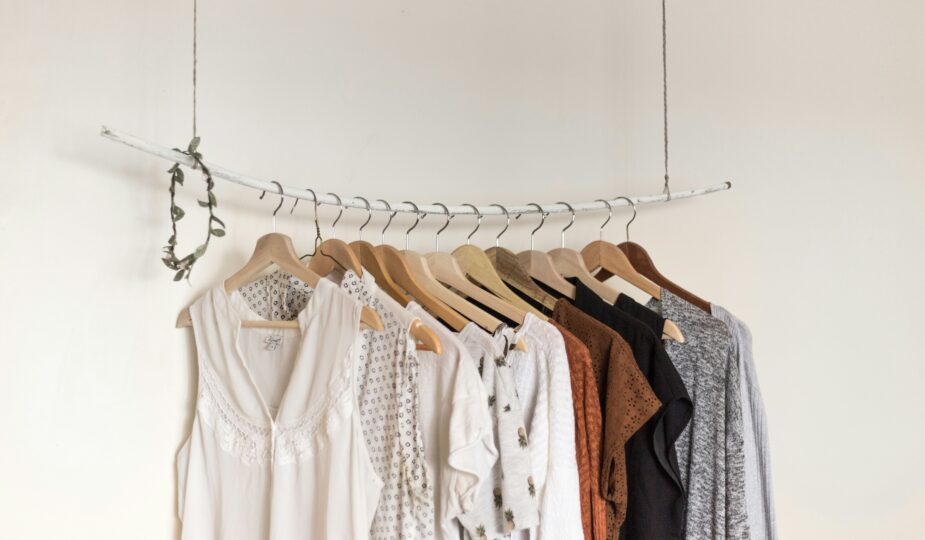A collection of neutral-toned women’s clothing displayed on wooden hangers on a suspended white clothing rail.