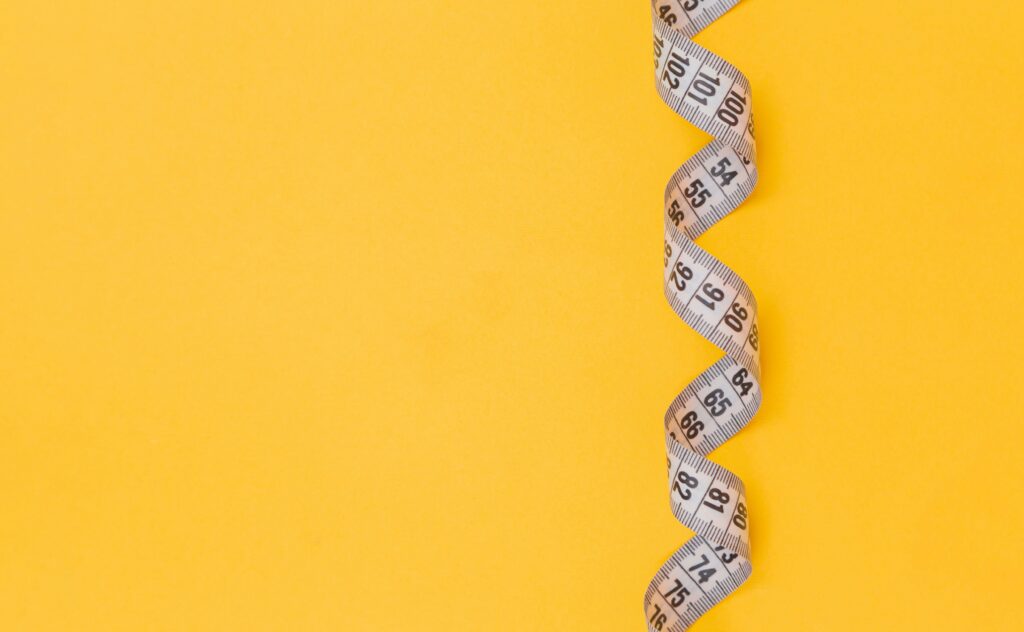 Measuring tape on a yellow background representing weight loss goals, budgeting, and mindful shopping decisions.